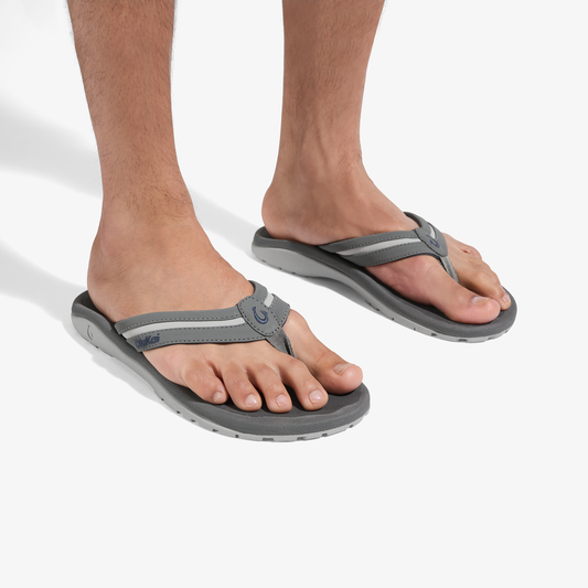 Man wearing grey and charcoal thong sandals with curved footbeds, viewed from front on white background.