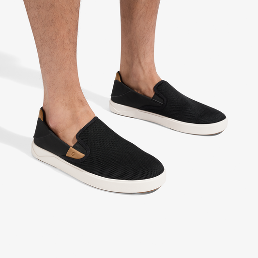 Black mesh slip-on sneakers with tan accent details and white rubber sole, worn on feet.