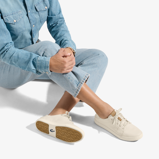 Cream canvas sneaker with lace-up closure and textured sole, worn with light blue denim shirt and jeans.