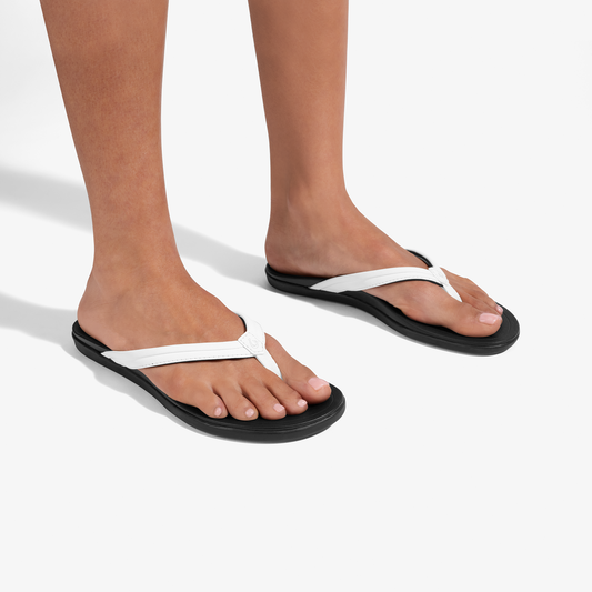 Pair of white and black thong-style sandals with black soles worn on bare feet.