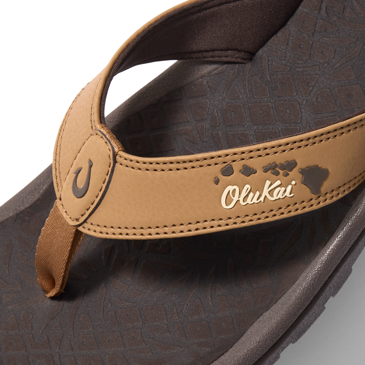 Tan and dark brown flip-flop with OluKai branding and island chain pattern on footbed.