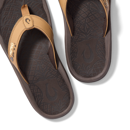 Tan and dark brown flip-flops with patterned footbeds and decorative toe straps, shown from above.