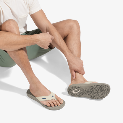 Man wearing white shirt and olive shorts sitting with clay-colored flip-flop sandal with textured sole visible.