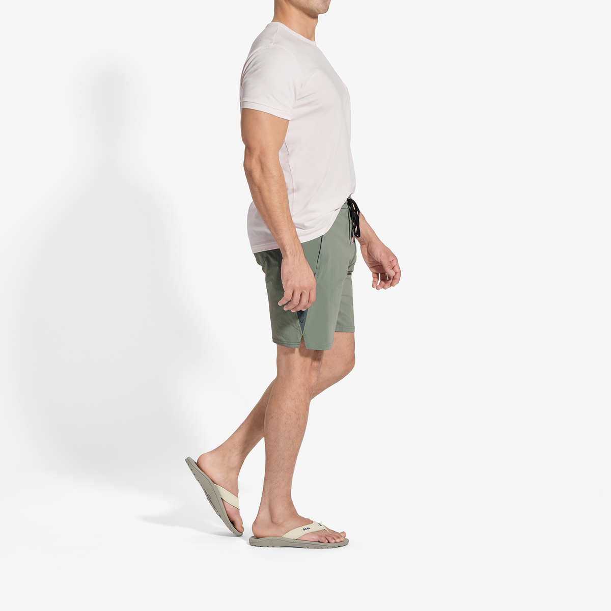 Man wearing white short-sleeve t-shirt, sage green shorts with drawstring, and tan slide sandals.