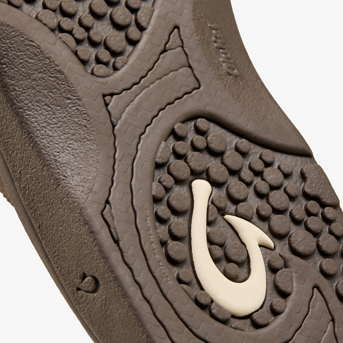 Dark wood sole with textured surface, studded pattern, and cream-colored hook-shaped emblem detail.