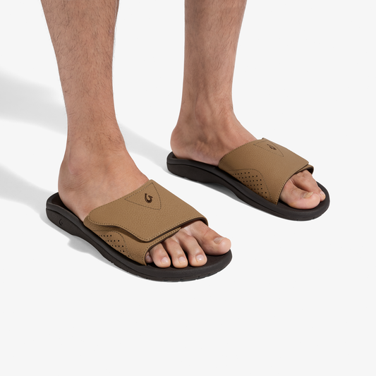 Tan and dark brown slide sandals with perforated upper and black sole, worn on feet.