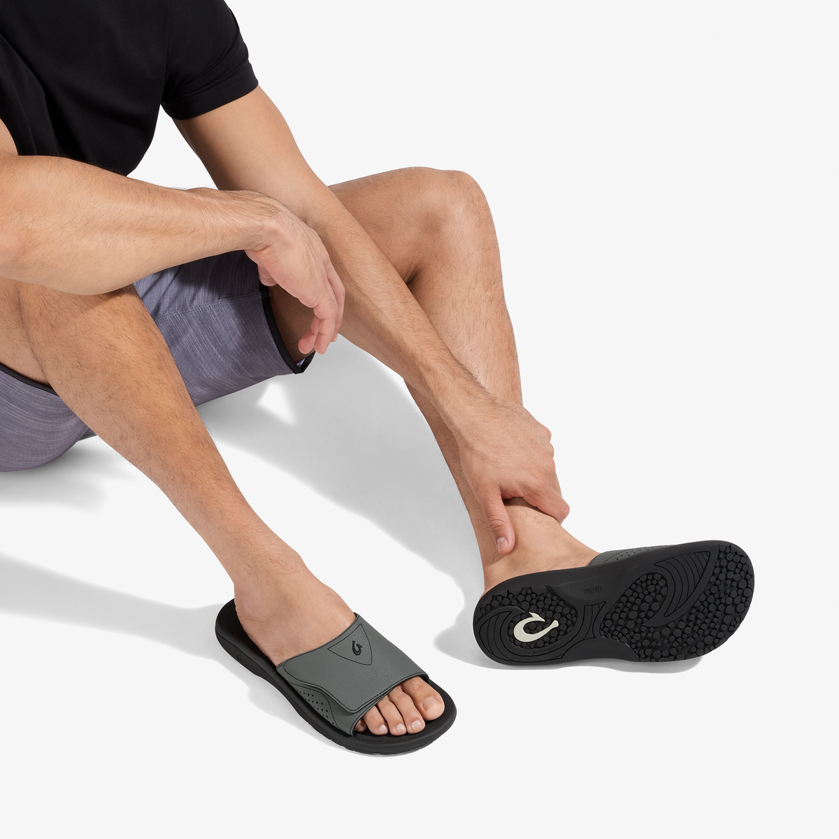 Man wearing gray and black slide sandal with textured sole and curved straps.
