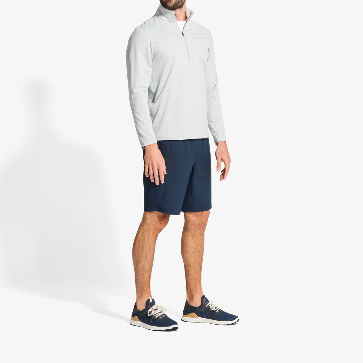 Man wearing natural quarter-zip long-sleeve pullover and trench blue shorts with navy sneakers.