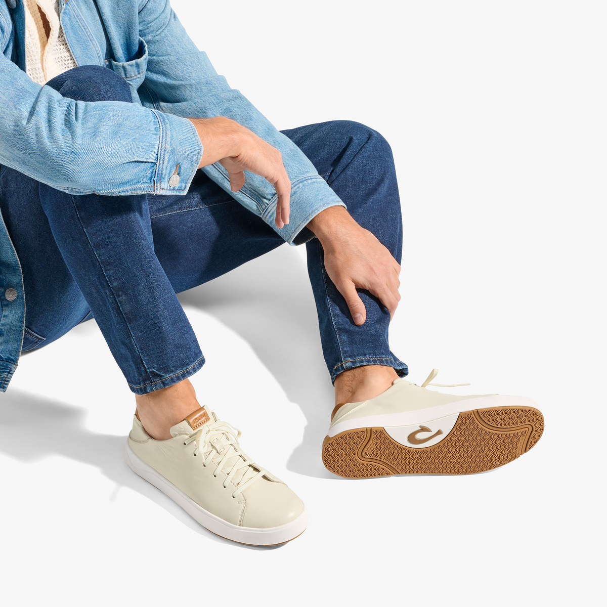 Cream canvas sneaker with white sole and tan rubber heel, worn with light blue denim shirt and dark jeans.