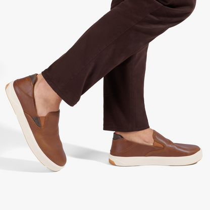 Brown leather slip-on sneakers with cream rubber soles worn with dark brown pants.