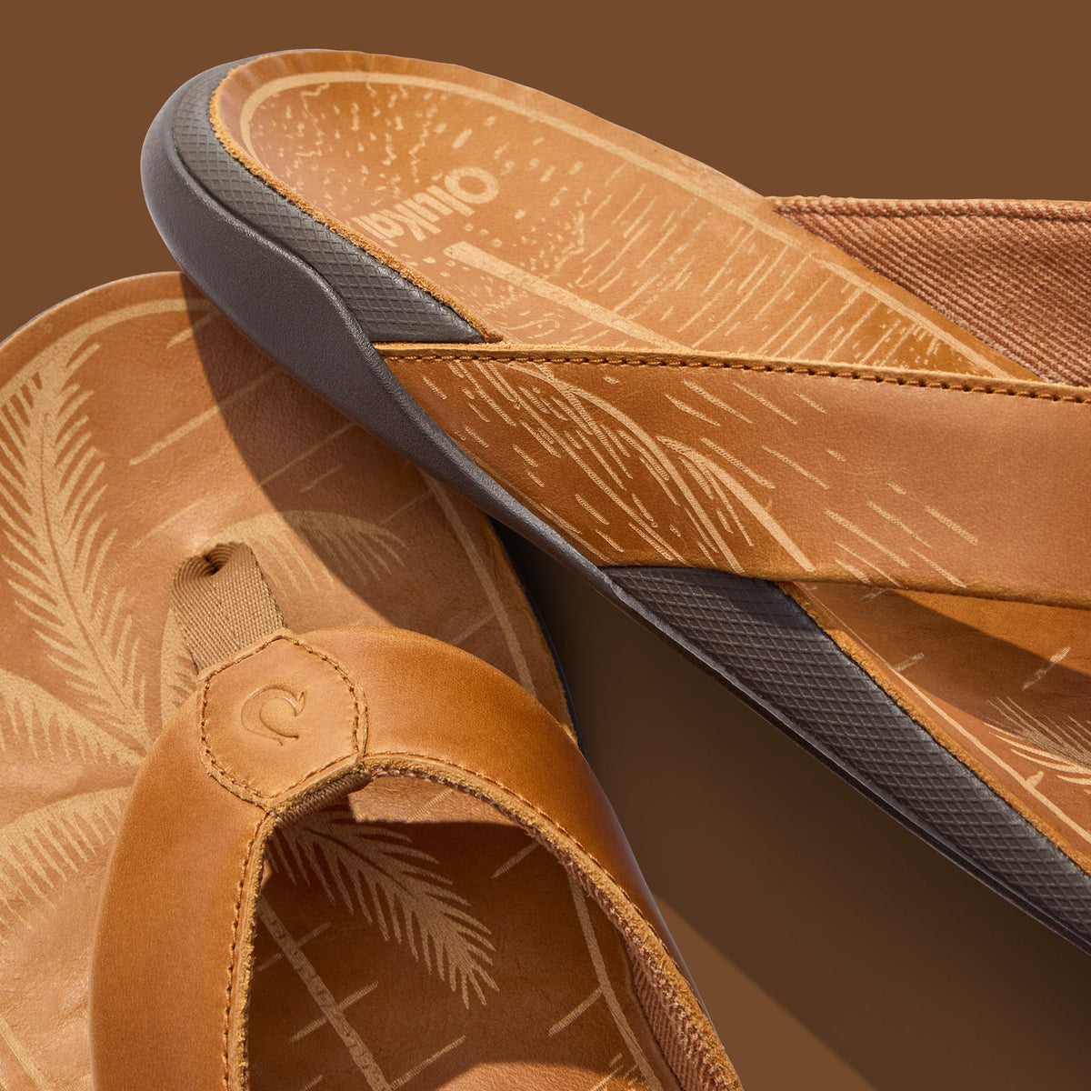 Tan leather slip-on shoes with gray rubber soles and embossed palm leaf pattern lining, displayed from above.