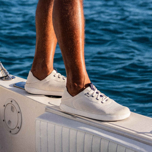 White mesh sneakers with navy laces on a boat deck overlooking ocean water.