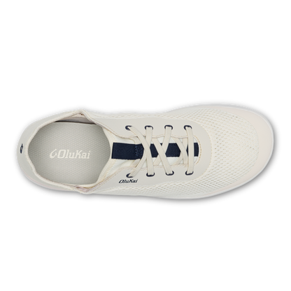 White canvas sneaker with dark blue laces and tongue, viewed from above showing perforated upper and Olukai branding.
