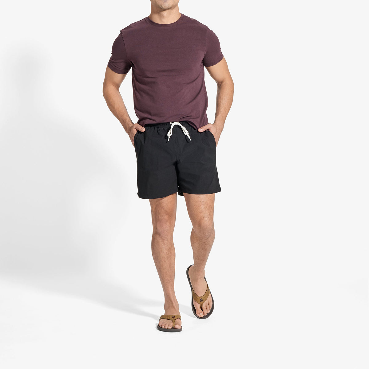 Man wearing dark burgundy t-shirt and black shorts with drawstring waistband and sandals.