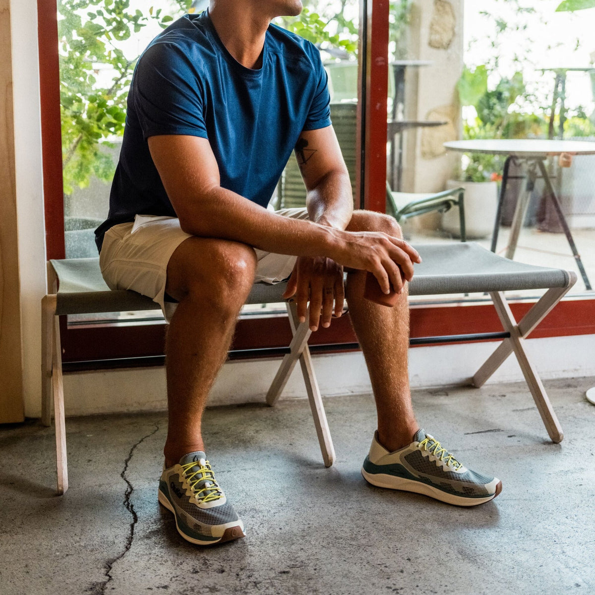 Man wearing seagreen short-sleeve t-shirt and cream shorts sitting on bench indoors.