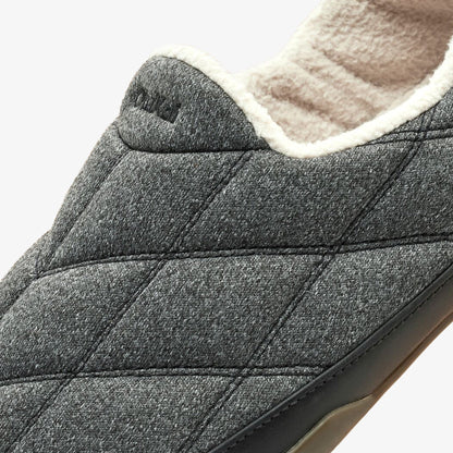 Dark gray quilted slipper with cream fleece lining and dark sole, close-up of heel and upper portion.