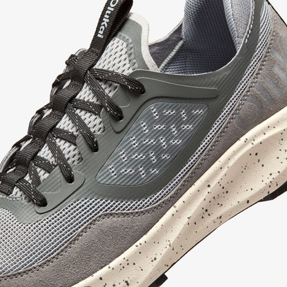 Gray and cream athletic shoe with black laces, mesh upper, and speckled sole detail shown from side angle.
