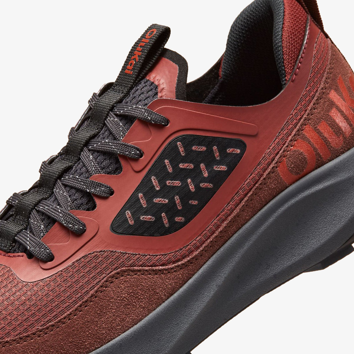 Red clay and carob athletic shoe with black laces, perforated panels, and gray sole detail.