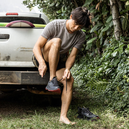 Man sitting on truck bed putting on black athletic shoes with red sole accents.