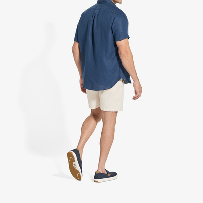 Man wearing blue short-sleeve shirt and tan shorts with navy slip-on shoes, shown from behind.