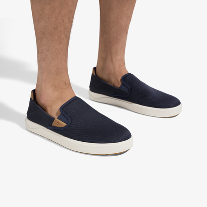 Navy blue slip-on sneakers with tan accents and cream rubber sole, shown on model's feet.