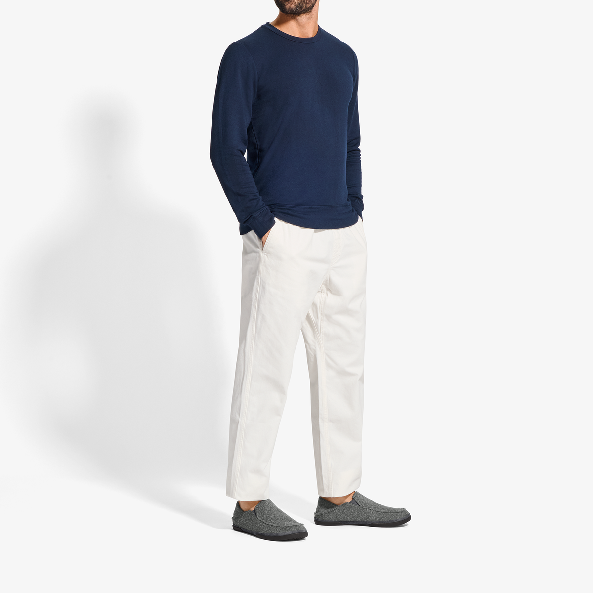 Man wearing dark navy long-sleeve sweatshirt, cream pants, and gray slippers.