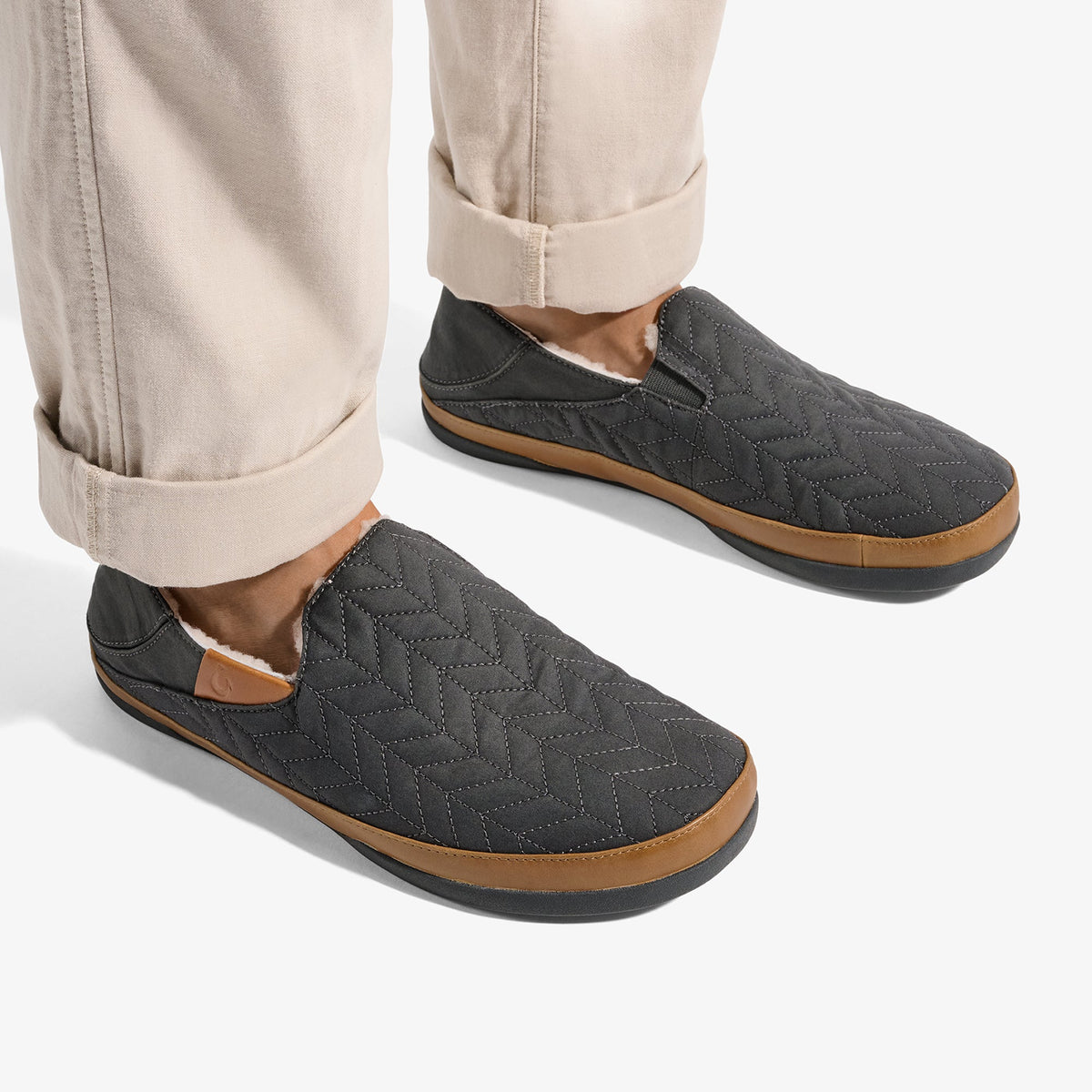 Dark gray quilted slip-on slippers with tan rubber soles, worn with rolled cream pants.