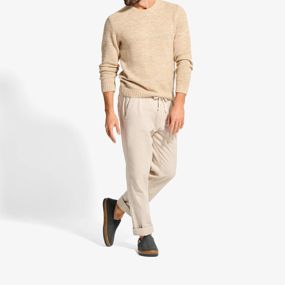 Man wearing beige crew neck sweater, cream drawstring pants, and dark suede slip-on shoes.