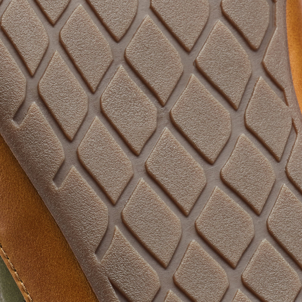 Beige textured sole with quilted diamond pattern, tan and green fabric visible at edge.