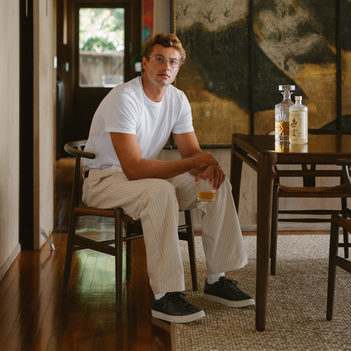 Man wearing lava rock lace-up sneakers with black and white sole while seated indoors.