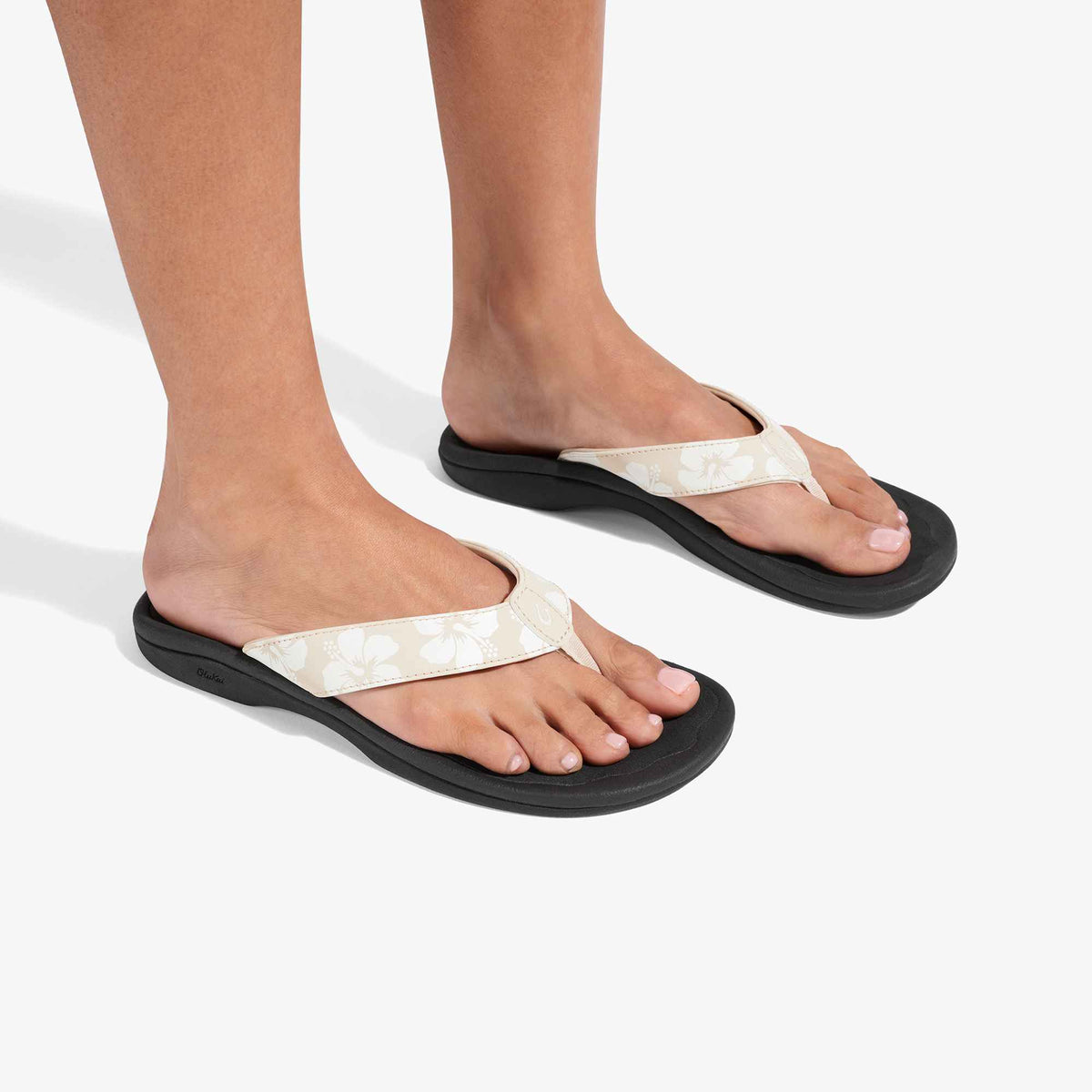 White and black flip-flop sandals with textured straps worn on feet against a white background.