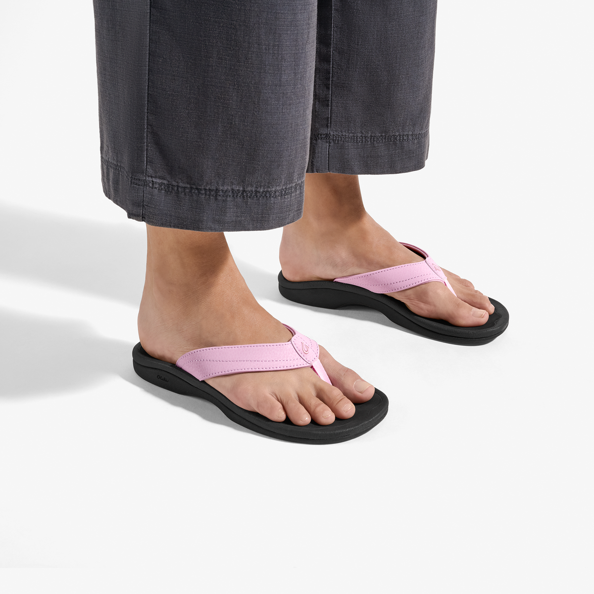 Person wearing pink flip-flops with black soles and gray cropped jeans.
