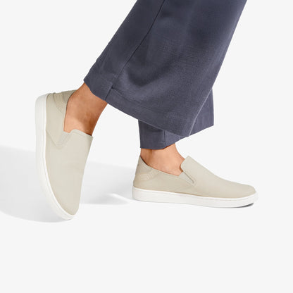 Cream leather slip-on shoes with white sole worn with dark blue pants.