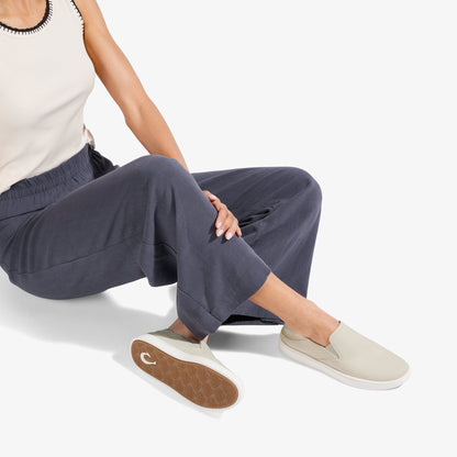 Cream leather slip-on sneaker with white sole, shown worn with dark pants.