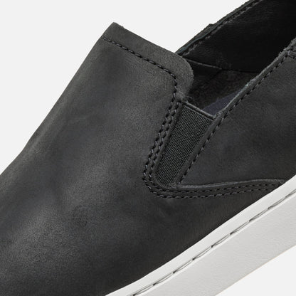 Black leather slip-on shoe with elastic gore detail and white sole, shown in close-up side view.