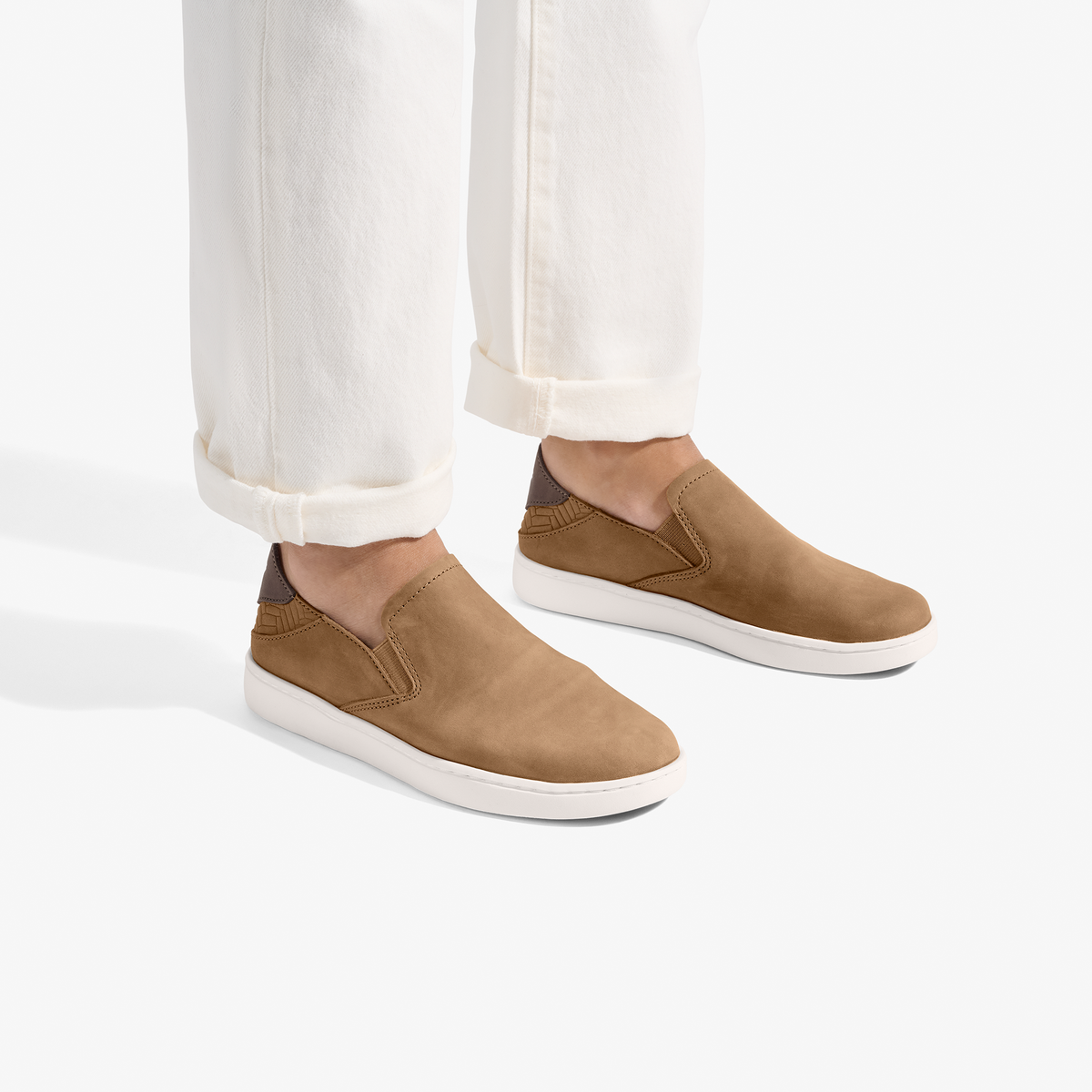 Tan leather slip-on shoes with white soles worn with cream-colored rolled pants.