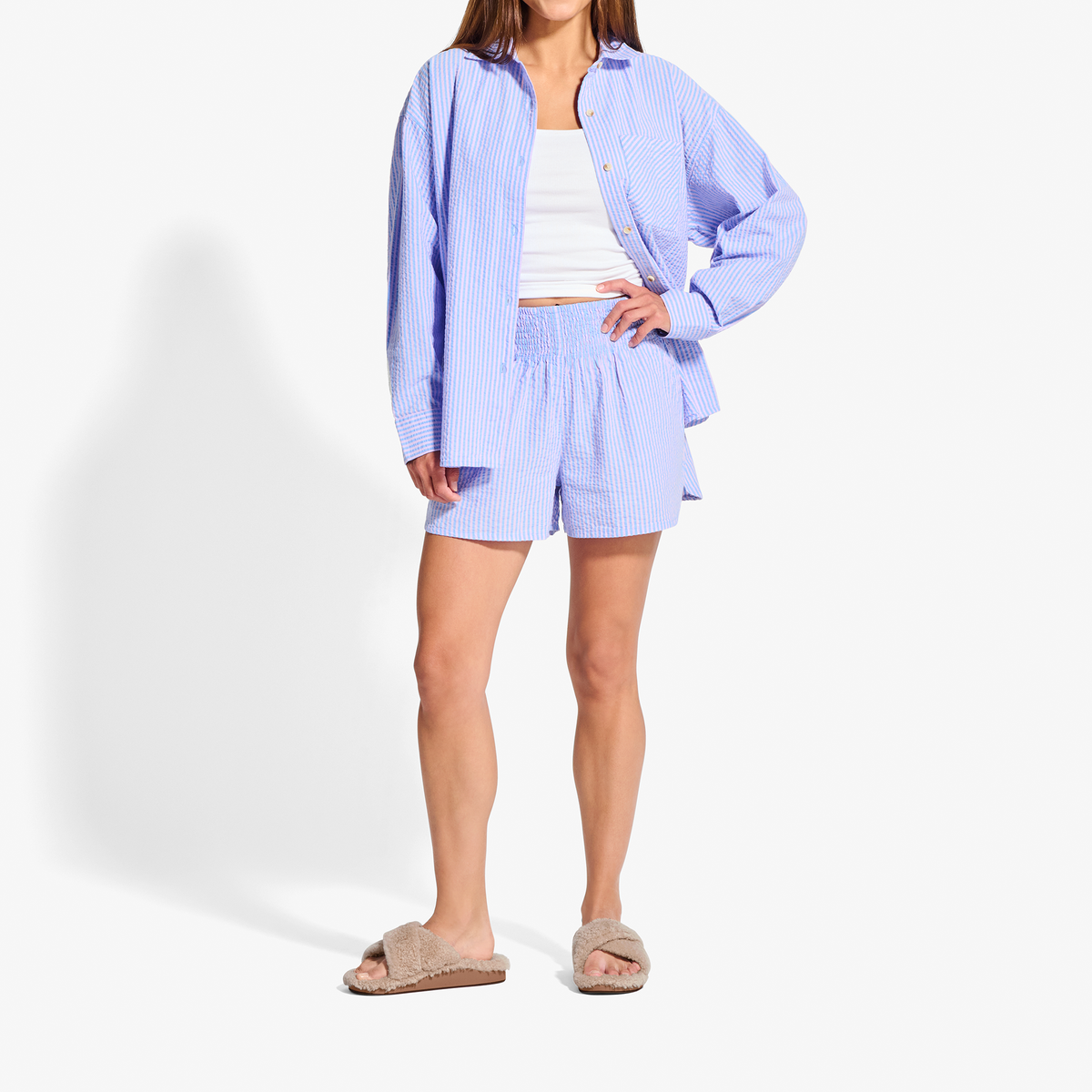 Woman wearing lavender striped button-up shirt and matching shorts with white tank top and tan slides.