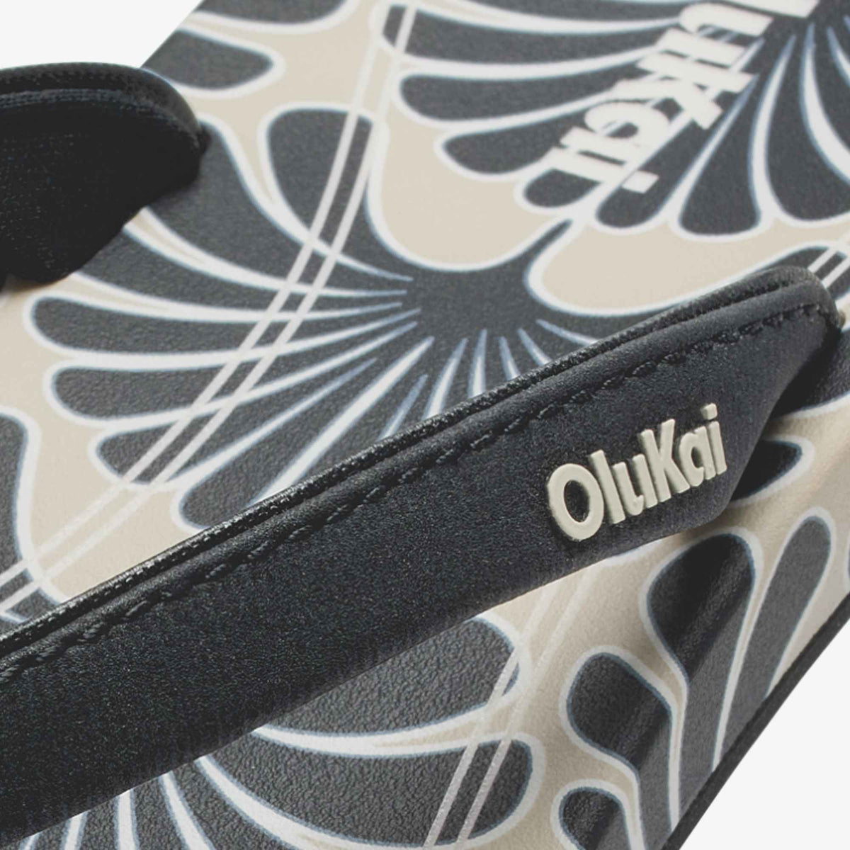 Black and cream patterned pouch with "oluKai" branding and geometric shell-inspired design.