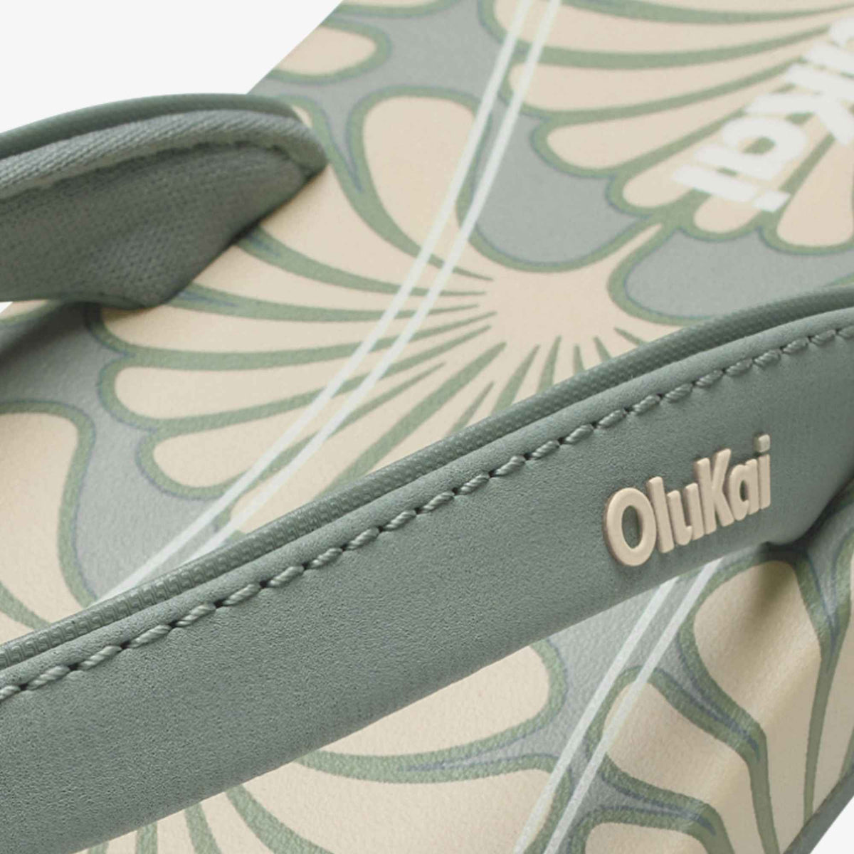 Close-up of gray-green and cream patterned bag with "Olukai" branding on leather strap.