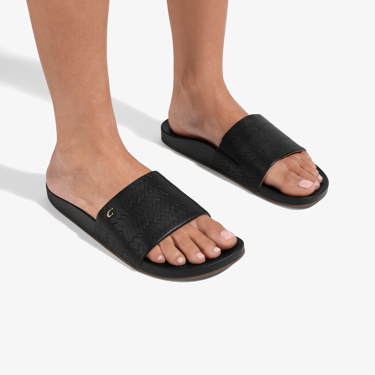 Black woven slide sandals with textured upper straps worn on feet against white background.