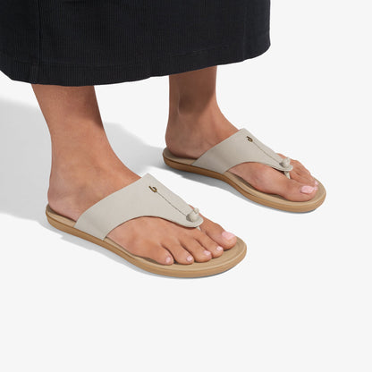 Warm sand-colored thong sandals with tan sole and metal accent detail, worn on feet.