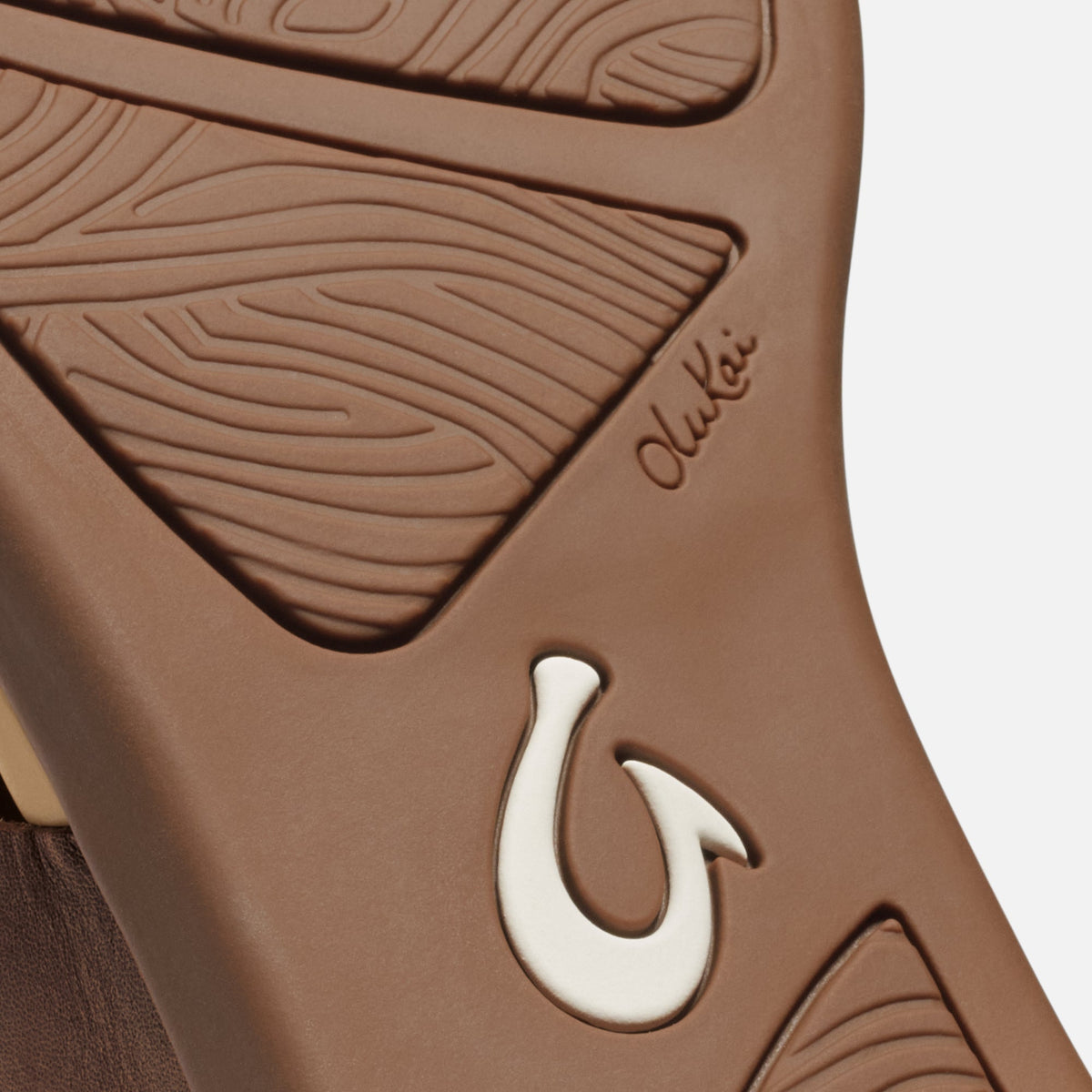 Toffee-colored sole with embossed leaf pattern and white horseshoe detail, showing brand name "Olukai" on side.
