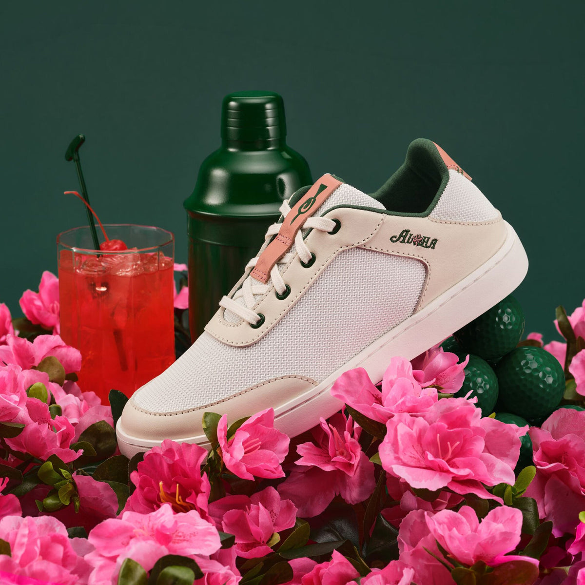 White canvas sneaker with coral laces and green heel tab, displayed among pink flowers and tropical styling props.
