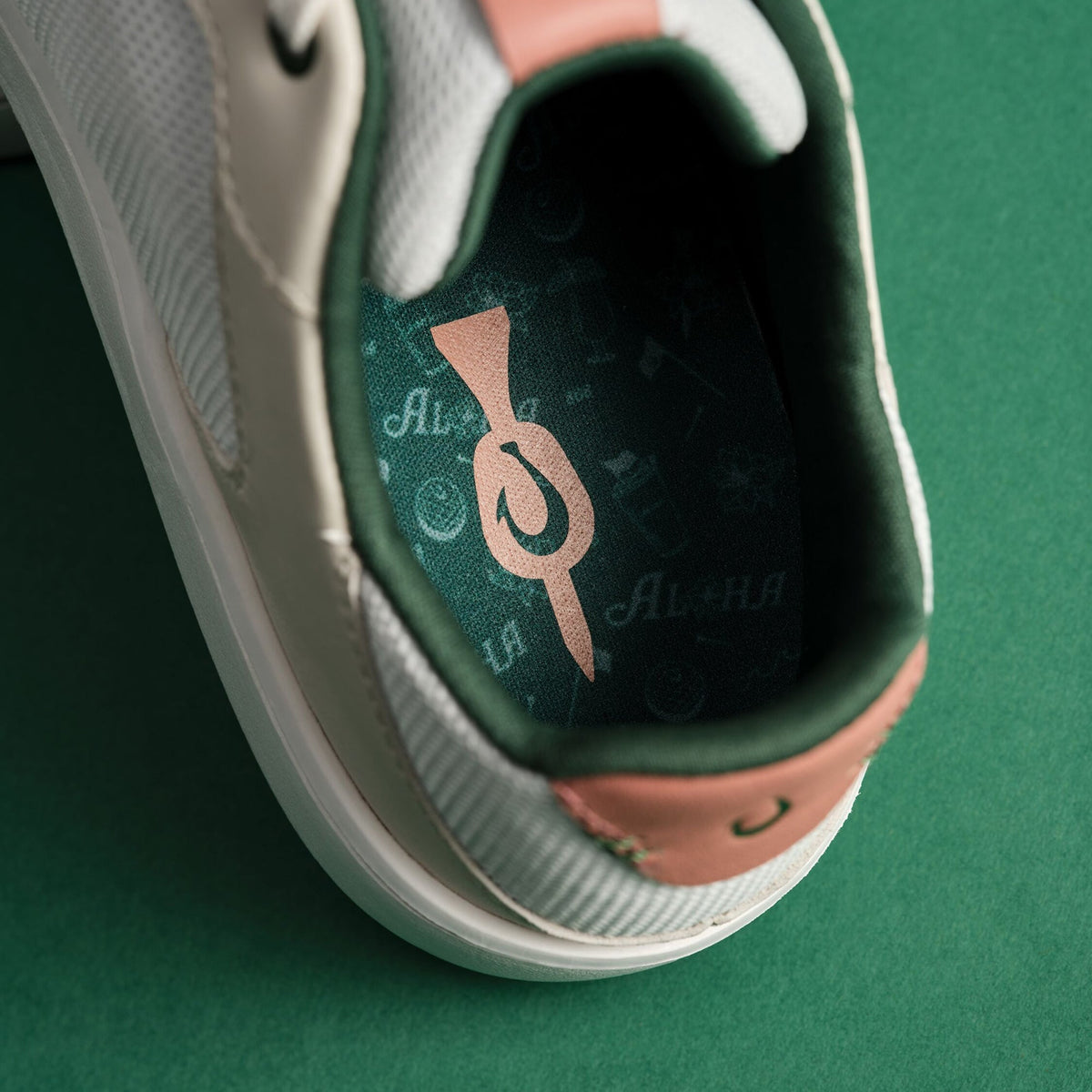 White slip-on sneaker with green and pink accents, showing white sole and decorative logo on green interior lining.