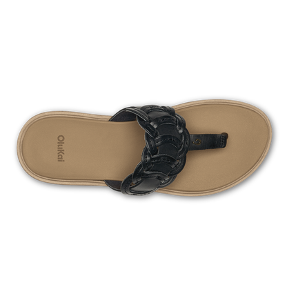 Flat lay of a black braided thong sandal with warm sand-colored sole, branded "Olukai" on footbed.