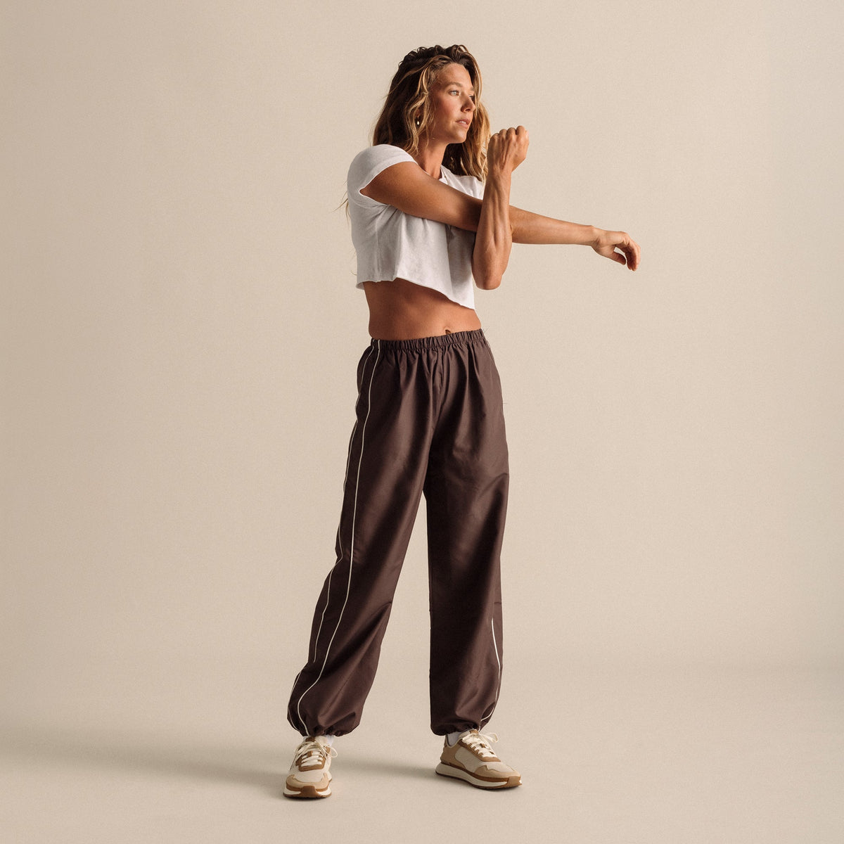 Woman wearing white cropped t-shirt and brown elastic-waist pants with cream sneakers.