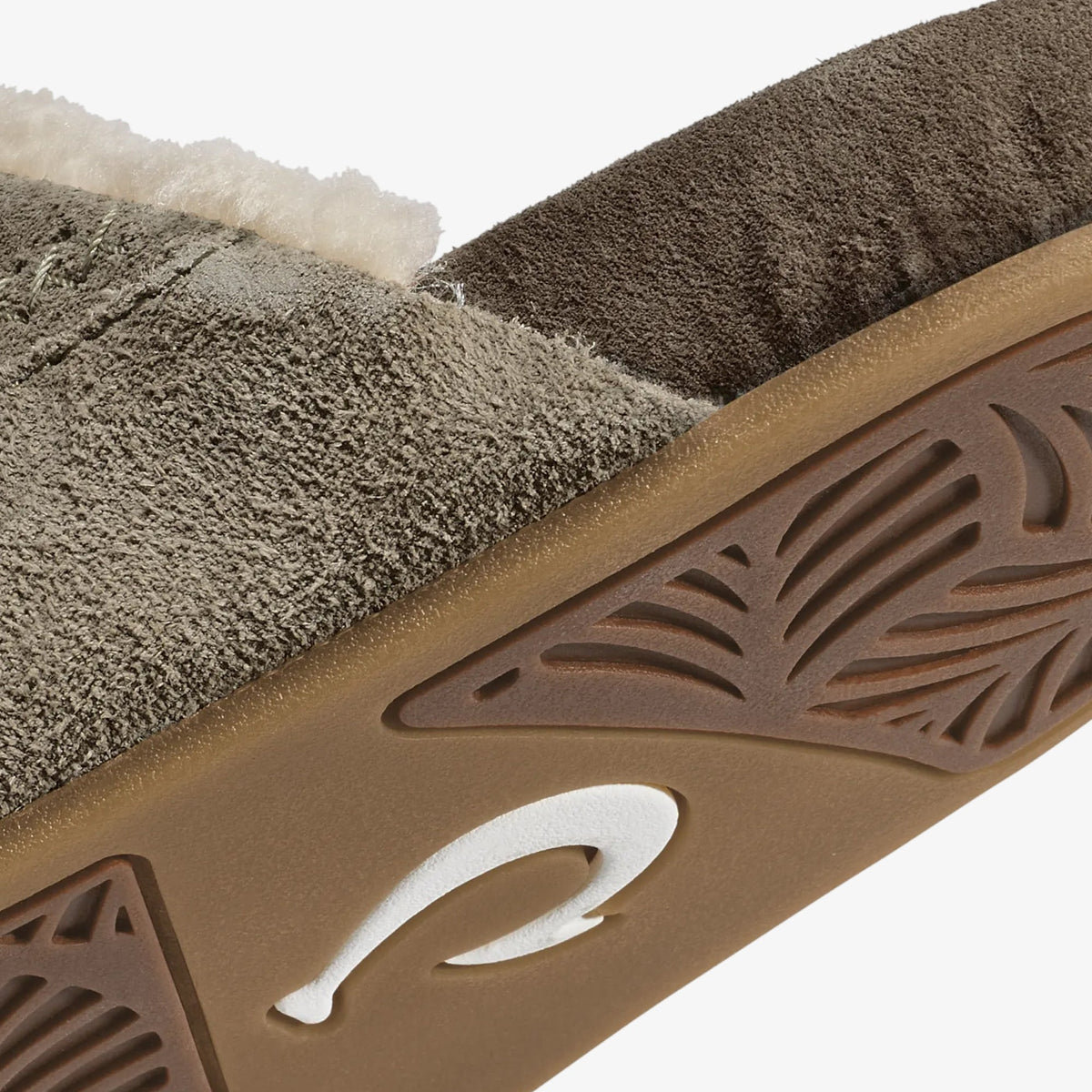 Textured slipper with tan suede upper, dark brown sole featuring carved designs, and white curved accent on the heel.