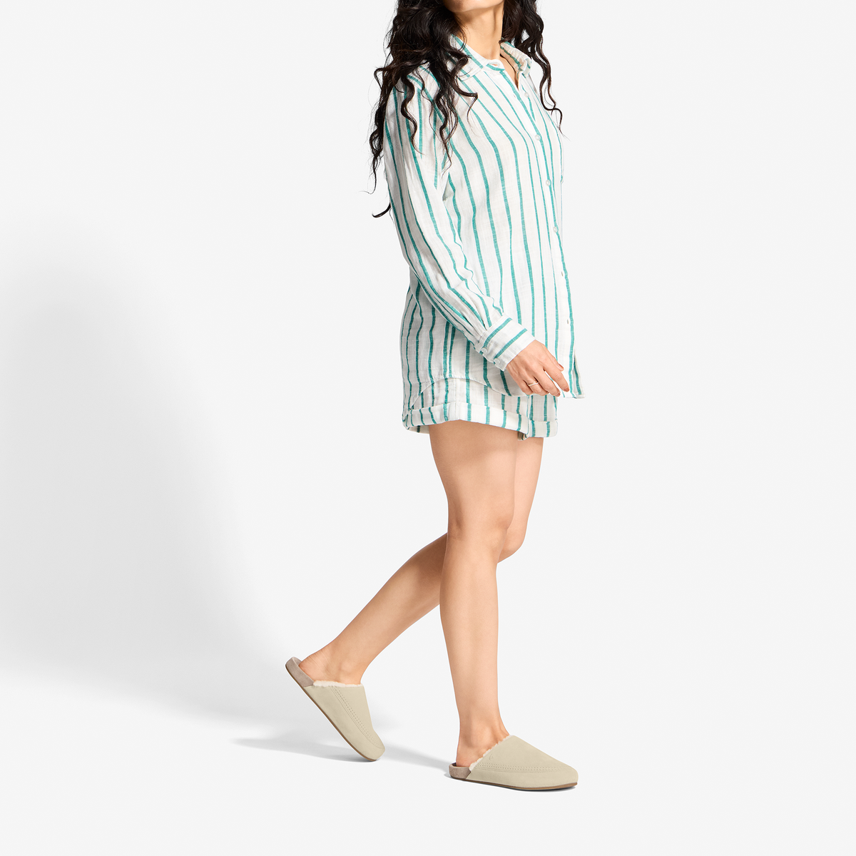 Woman wearing teal and white vertical striped button-up shirt dress with long sleeves and cream slip-on shoes.
