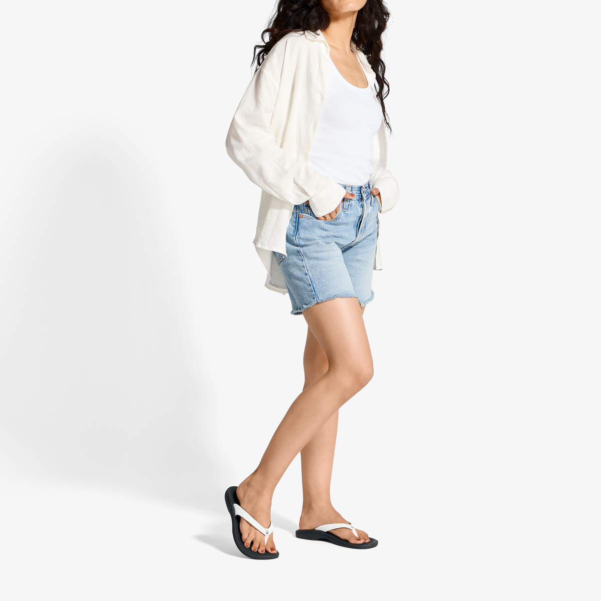 Woman wearing white cardigan, white t-shirt, light blue denim shorts, and black flip-flops.
