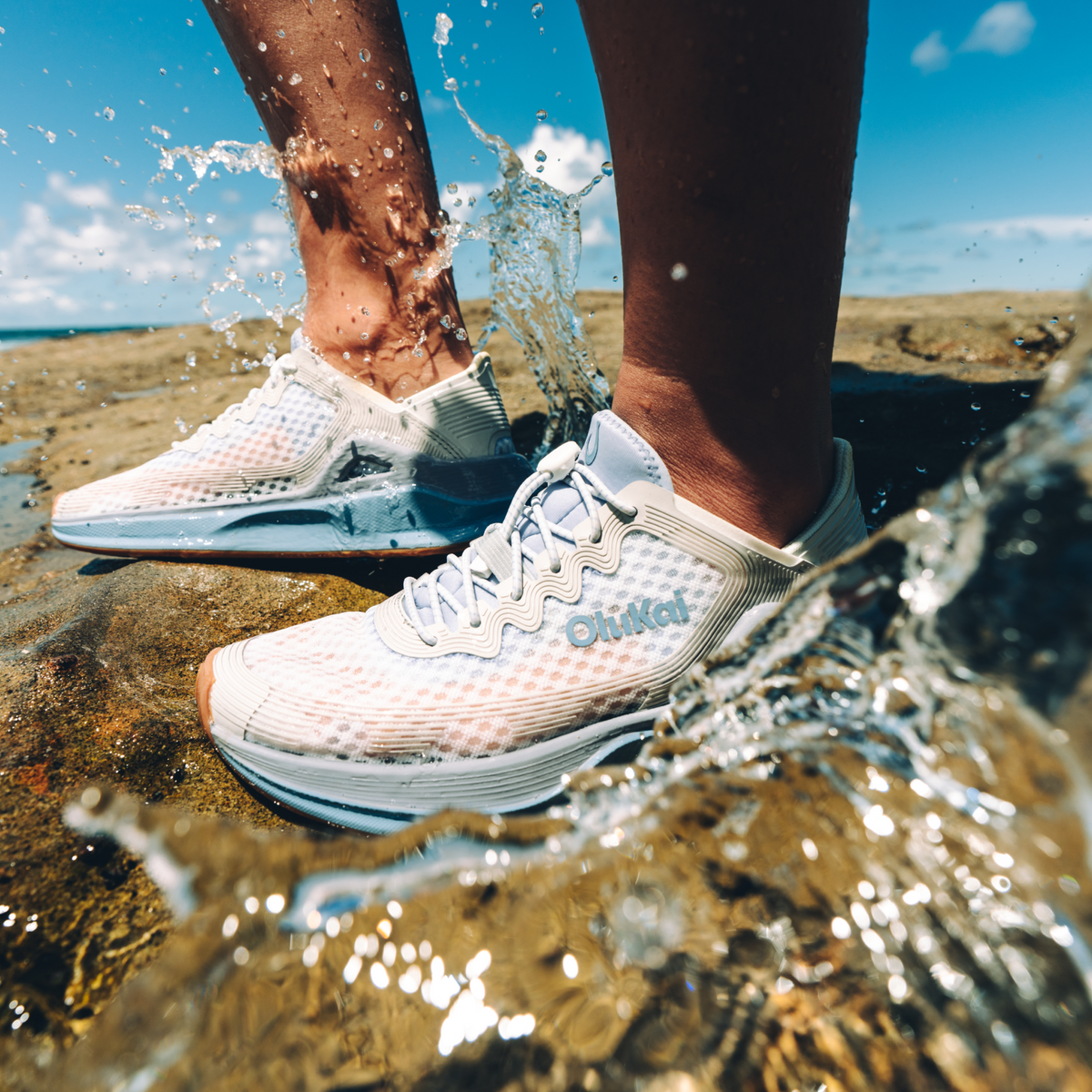 White and light blue mesh running shoes worn in shallow water on a beach.